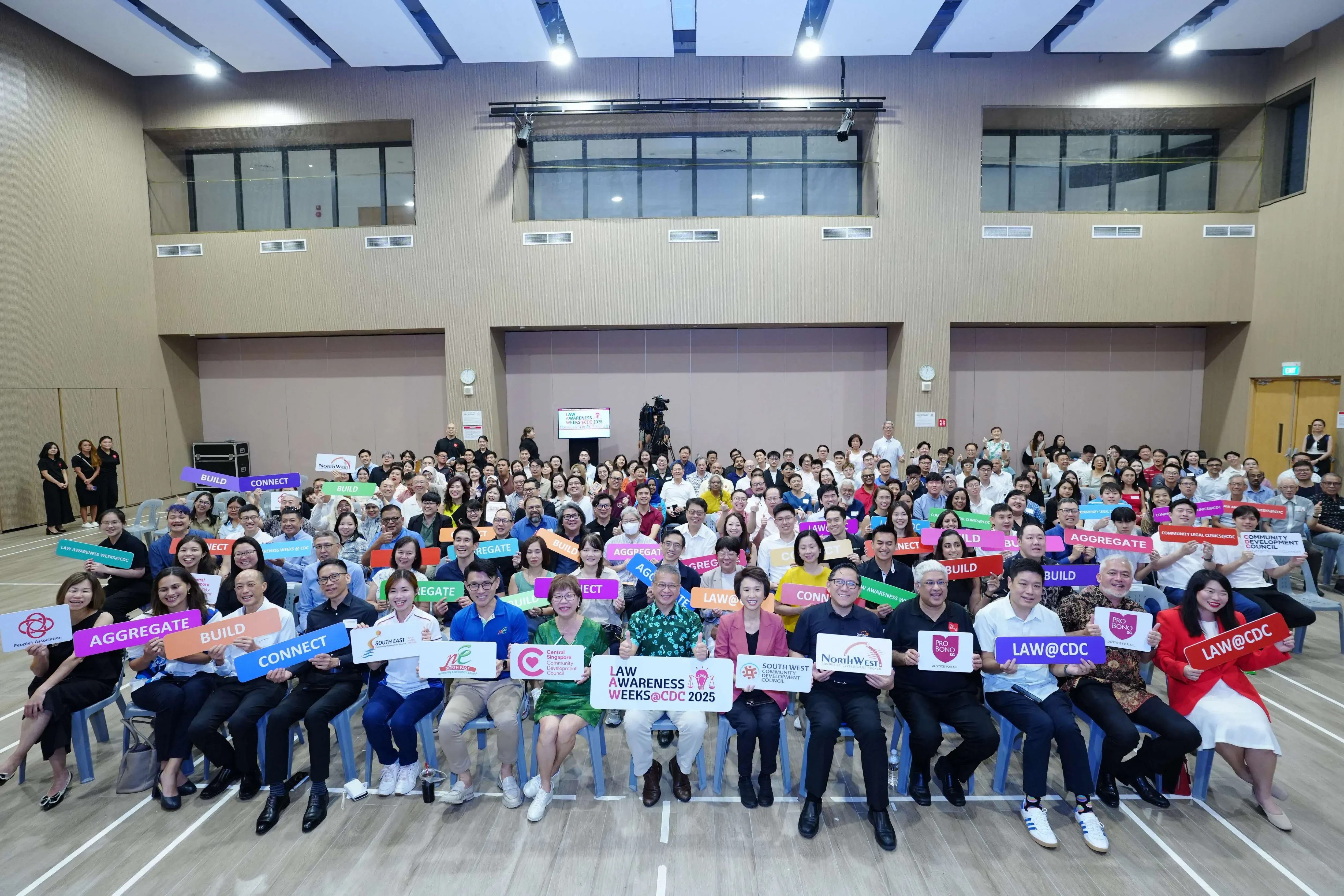 A group of people seated holding colorful signs with various messages such as "CONNECT", "AGGREGATE", and "CARING COMMUNITIES".